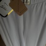 Zbliżenie na srebrne logo Sensual Woman i ekologiczną metkę białych spodni bawełnianych. detal 1