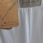 Zbliżenie na srebrne logo Sensual Woman i ekologiczną metkę białych spodni bawełnianych.
