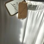 Zbliżenie na srebrne logo Sensual Woman i ekologiczną metkę białych spodni bawełnianych. Detal 3 tkanina