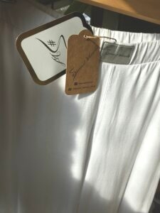 Zbliżenie na srebrne logo Sensual Woman i ekologiczną metkę białych spodni bawełnianych. Detal 3 tkanina