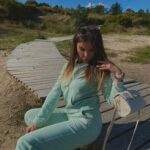Kobieta w miętowym komplecie dresowym z bawełny siedząca na drewnianej kładce z kremową torebką i okularami przeciwsłonecznymi Sensual Woman.