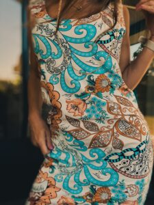 Bliskie ujęcie na wzorzysty materiał letniej sukienki z motywem paisley, turkusowymi i pomarańczowymi kwiatami oraz złotym łańcuszkiem