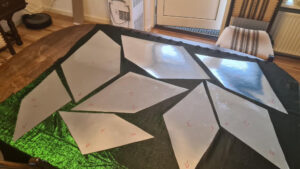 Wycięte elementy skrzydeł ułożone na połyskującym zielonym materiale.2