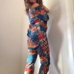 kobieta w pomarańczowych spodniach z wiązaniem, stylizacja z asymetryczną bluzką i szpilkami. poza tyłem.