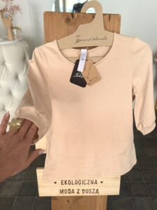 Dopasowana bluzka damska w kolorze ecru z ekologicznej bawełny na drewnianym wieszaku, krój slim fit, okrągły dekolt