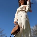 Elegancka stylizacja z beżowym dresem, wzorzystą chustą na głowie i okularami przeciwsłonecznymi.