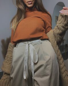 Dopasowany golf damski w kolorze cynamonowym w jesiennej stylizacji z beżowymi spodniami z logowaną wstążką i grubym kardiganem Sensual Woman.